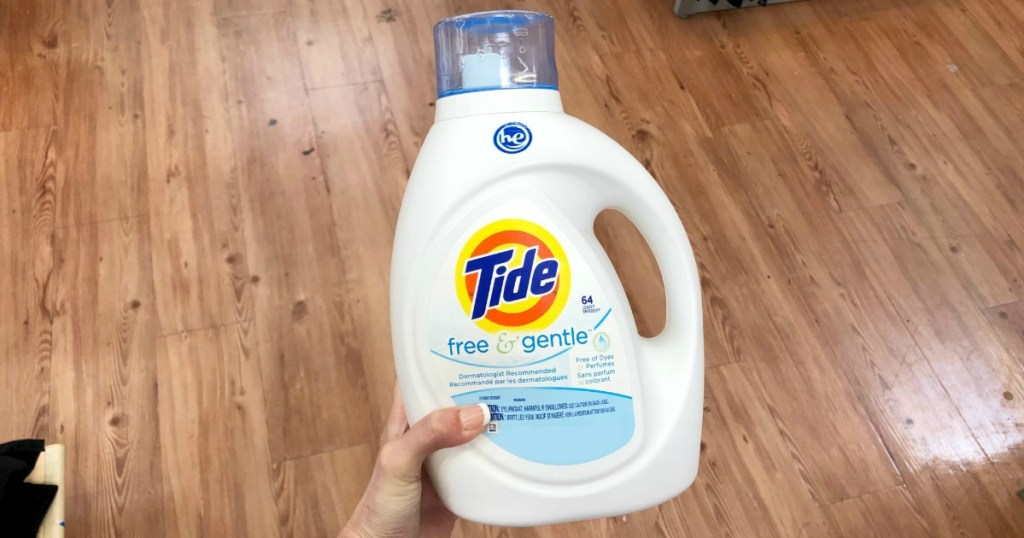 hand holding a bottle of tide laundry detergent above a polished wood floor