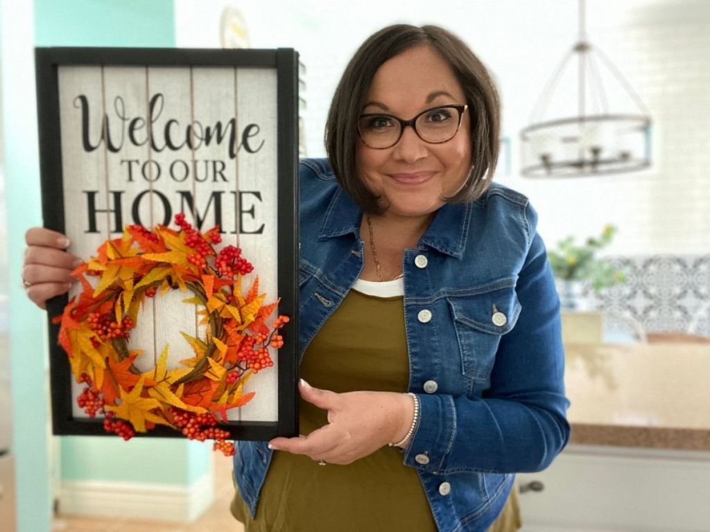 woman holding Welcome to our Home sign and hanging fall wreath