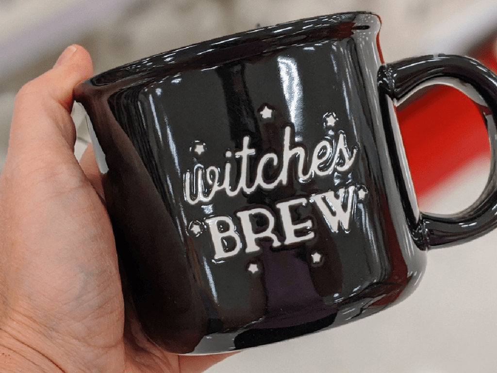 hand holding black mug with words "witches brew" on it