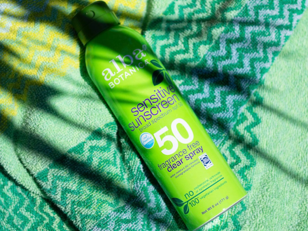 green bottle of sunscreen on patterned green towel with tree shadow