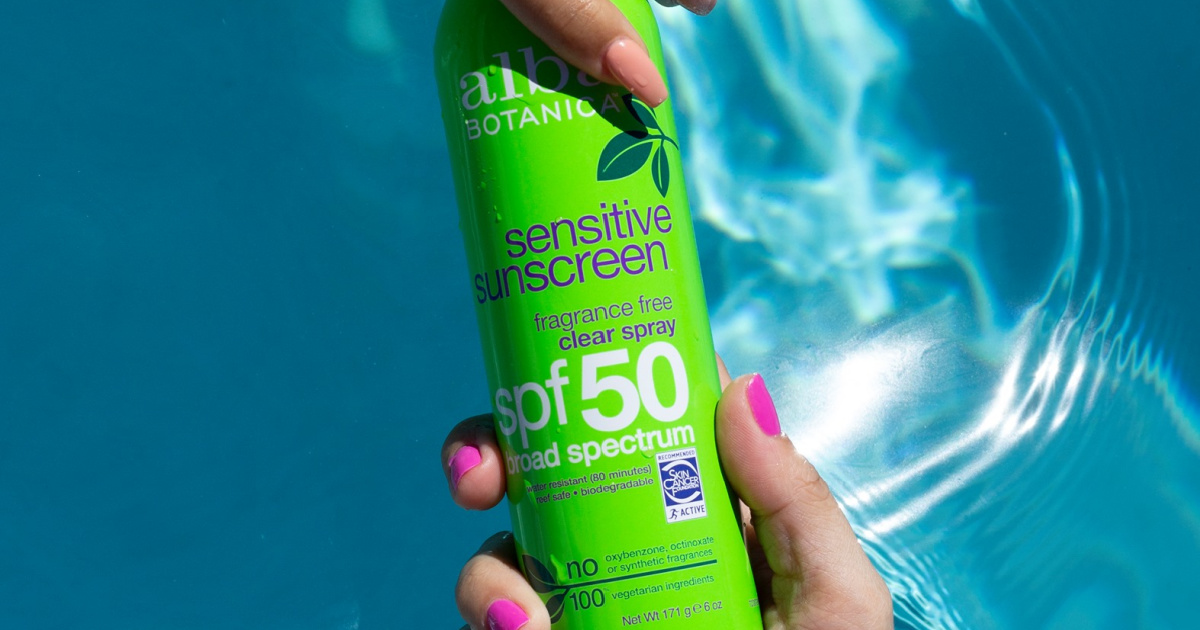 hands holding green bottle of sunscreen in pool water