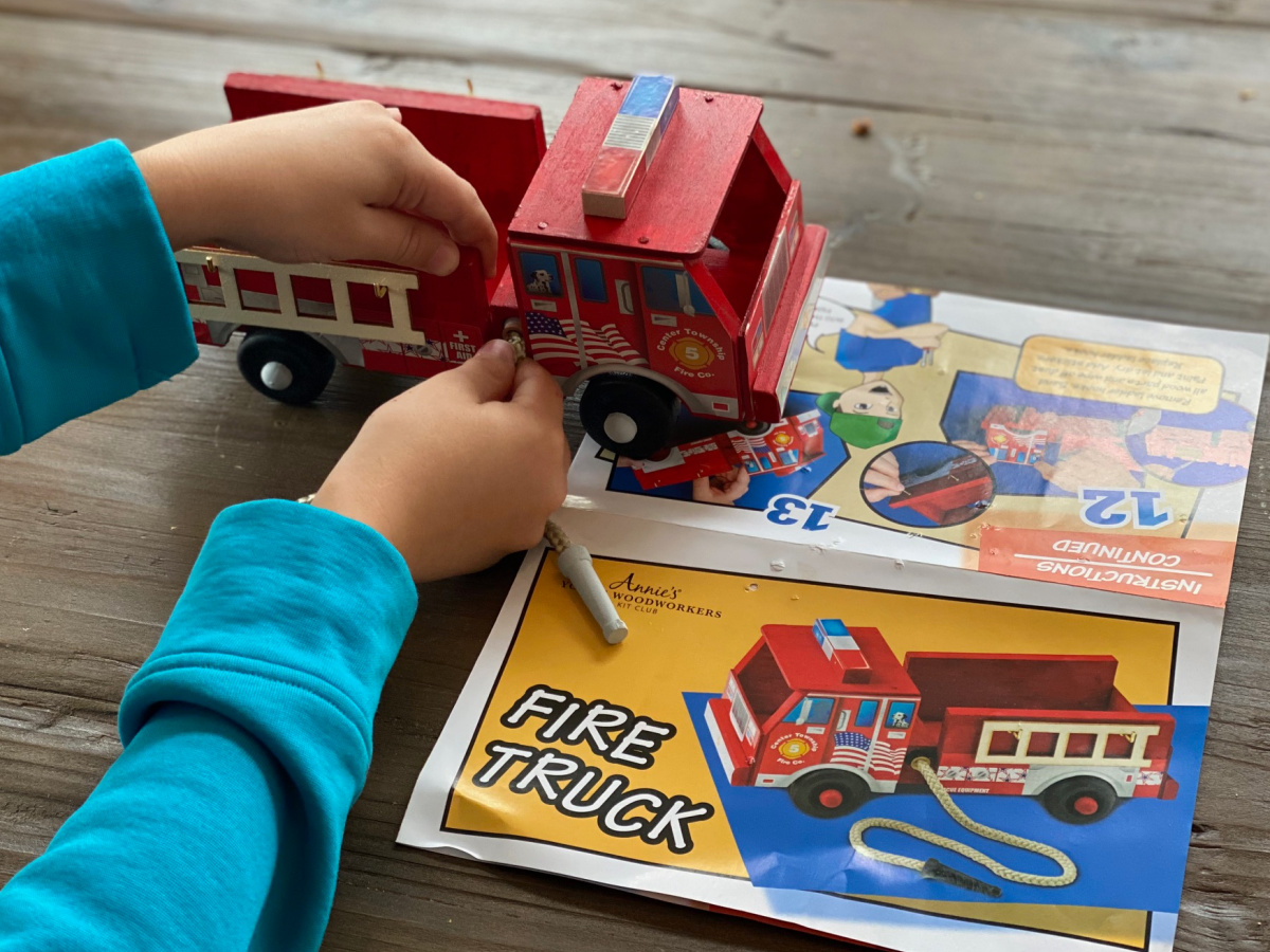 child's hand building a red wood fire truck