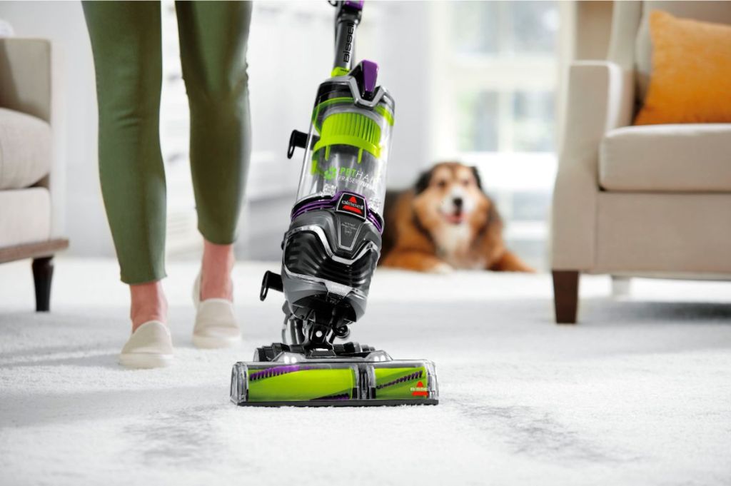 woman vacuuming with BISSELL Pet Hair Eraser Turbo Plus Lightweight Upright Vacuum Cleaner and dog in the background