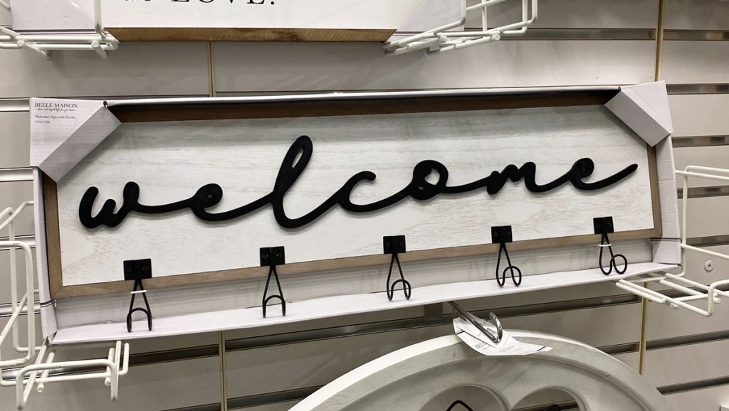 white sign that says welcome in black cursive font with black hooks along bottom of sign