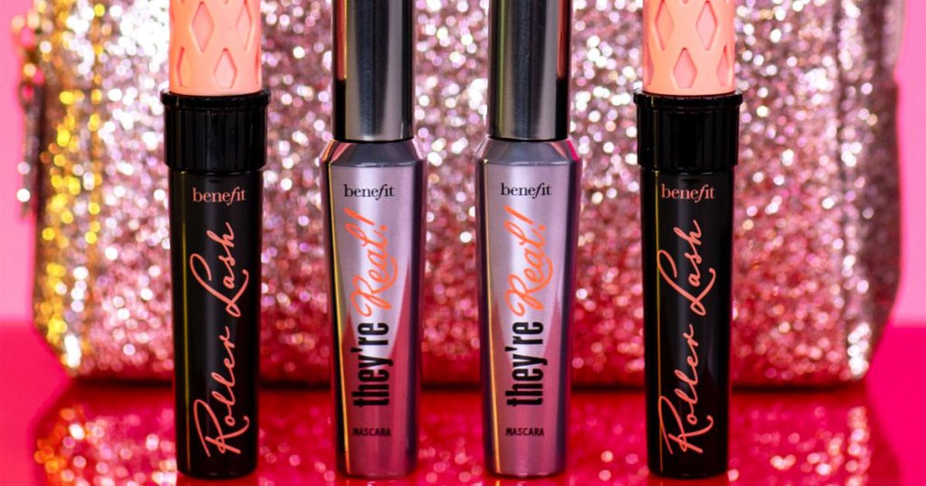 two benefit they're real and two roller ball mascara tubes in front of a pink sparkly makeup bag
