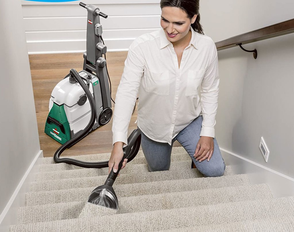 woman using carpet cleaning hose attachment to clean carpeting on stairs