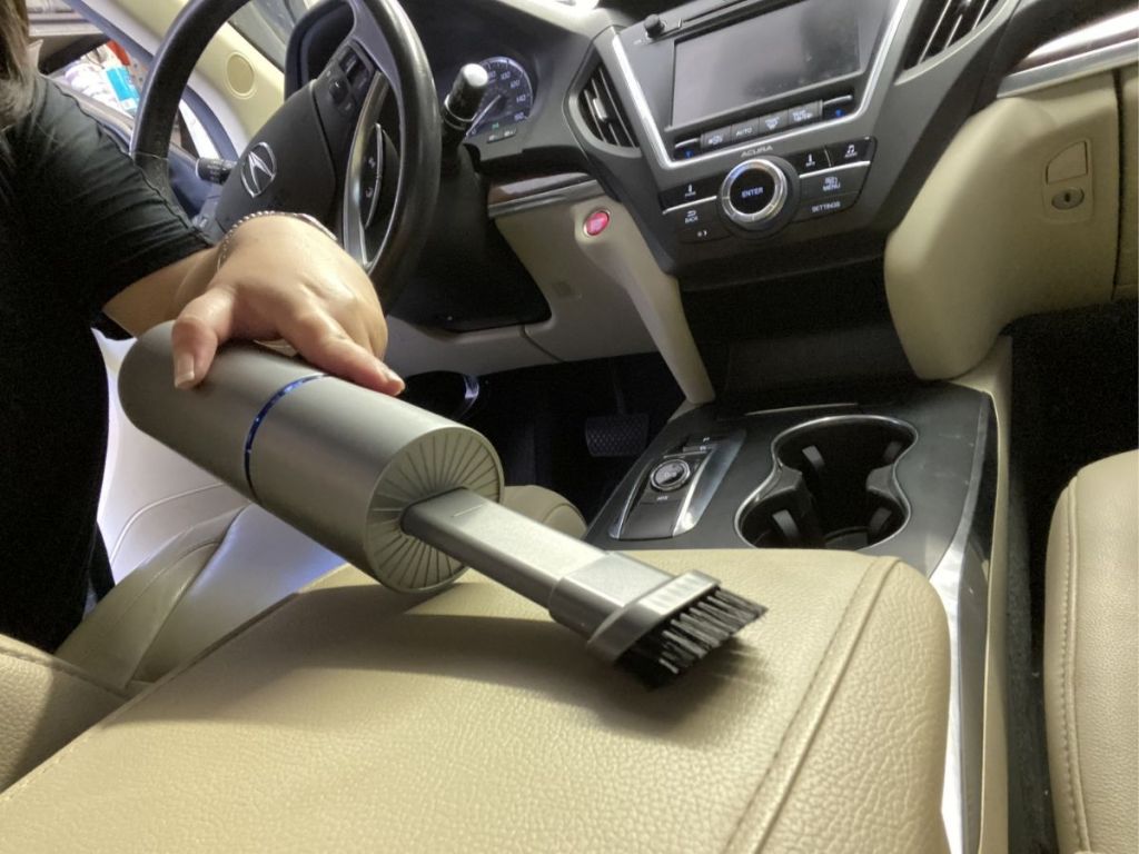 woman using mini vacuum to clean center counsel in car