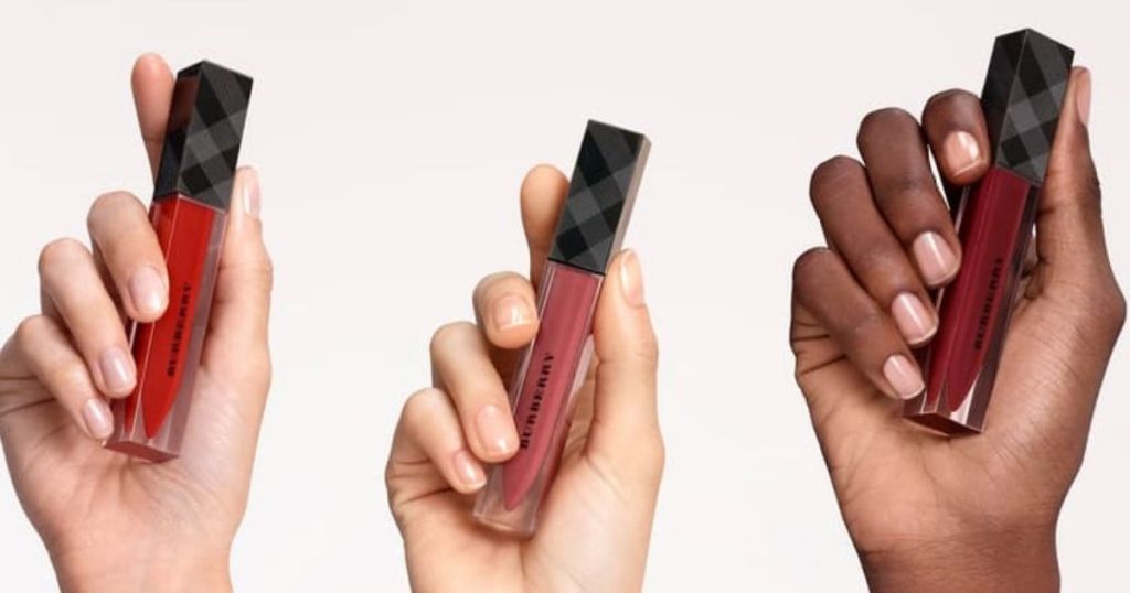 three hands holding Burberry lipglosses