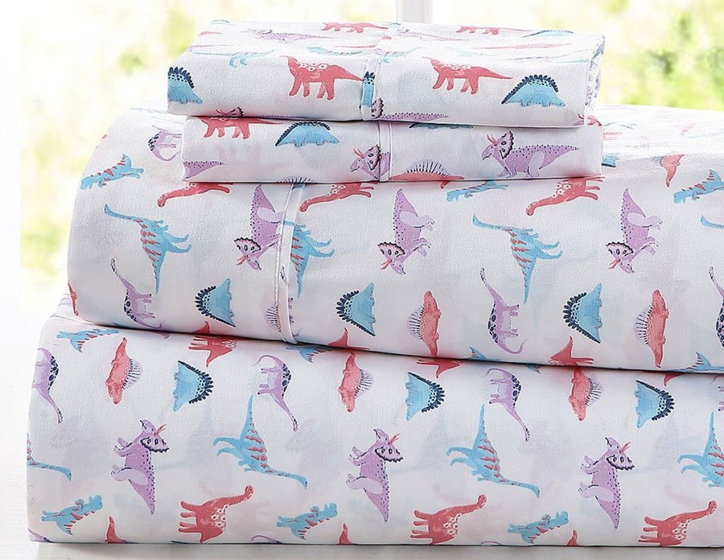 folded set of white sheets with pink, purple, and blue dinosaur print