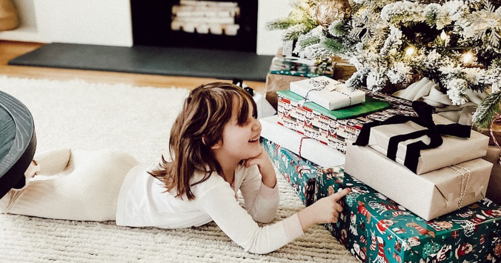 girl laying on belly pointing to gifts under christmas tree - 4 gift rule