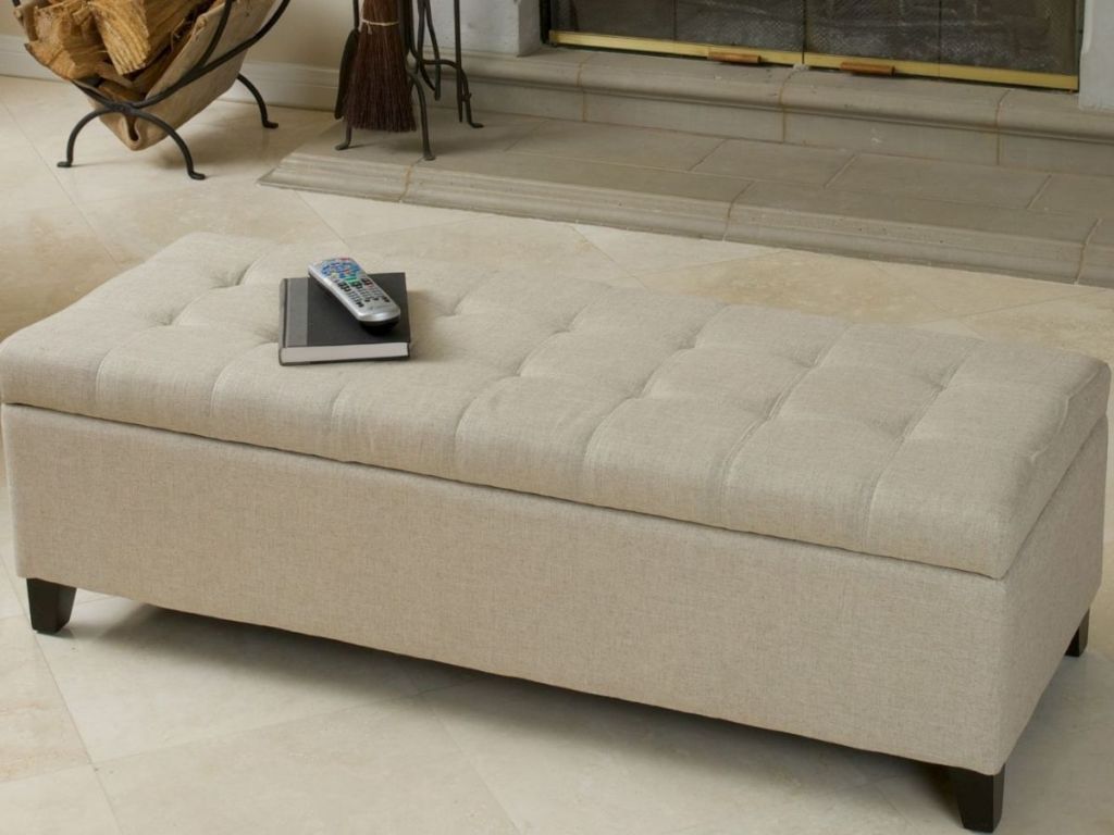 beige tufted ottoman with book and remote resting on it 