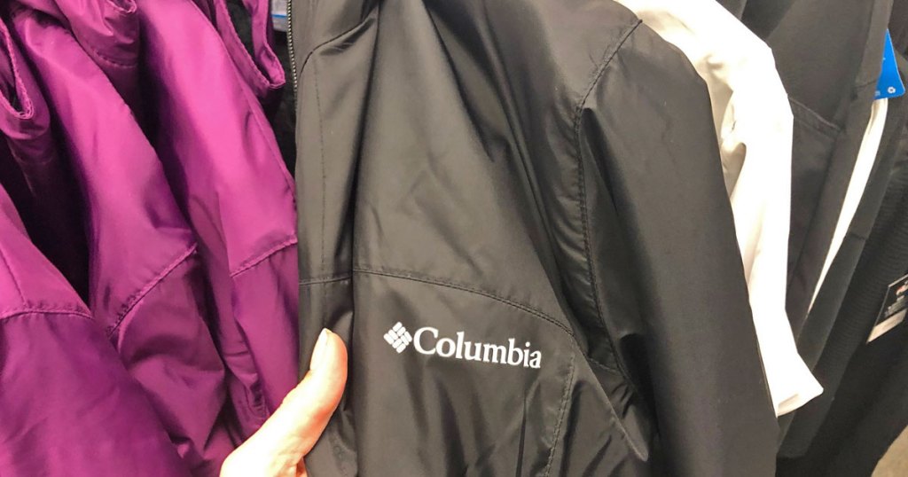 person holding a black columbia windbreaker jacket on rack of other jackets