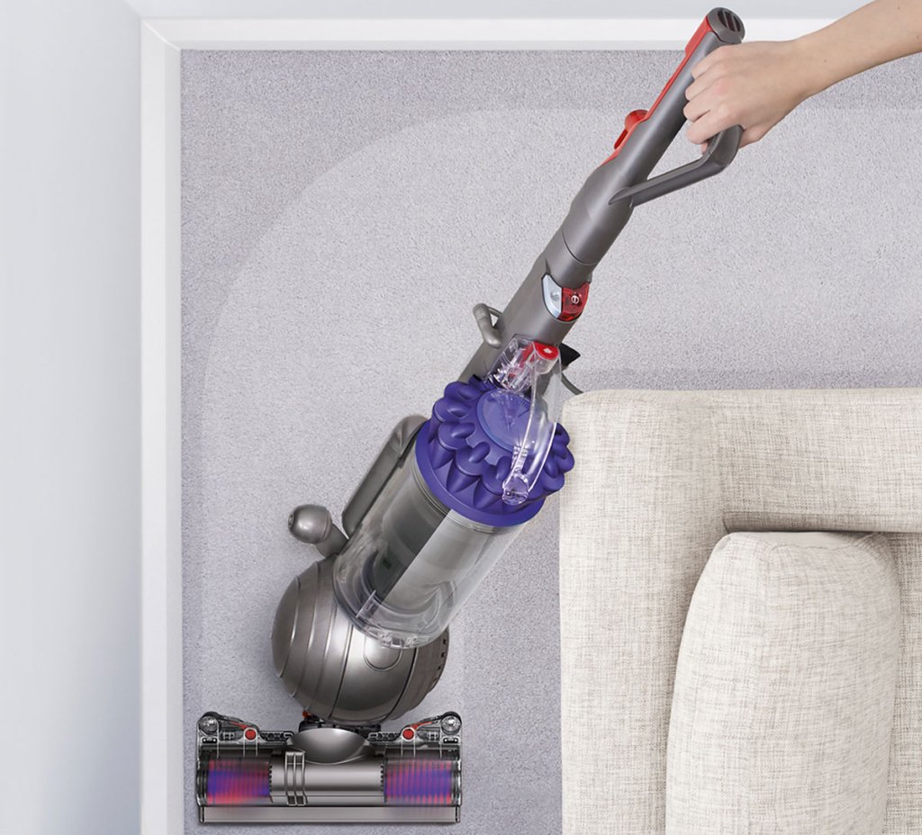 person using a grey and purple dyson vacuum on carpet around a couch
