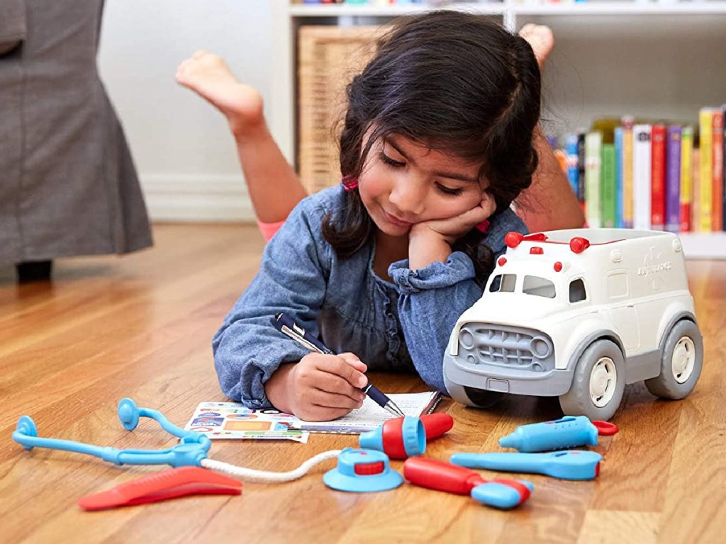 girl playing with toy ambulance and doctor accessories on hardwood floor
