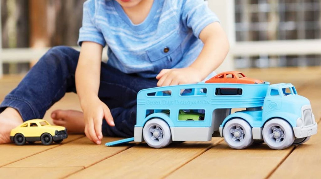 boy playing with a blue car carrier truck with three cars