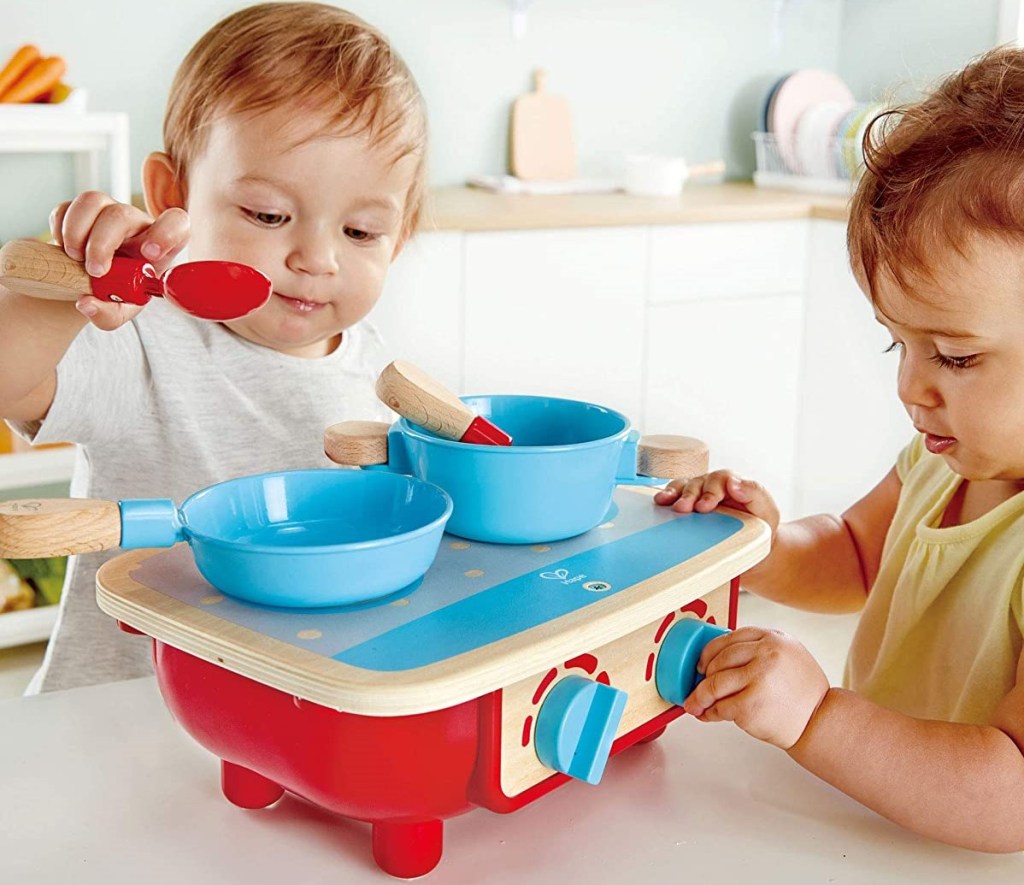 two toddlers playing with a wooden kitchen set