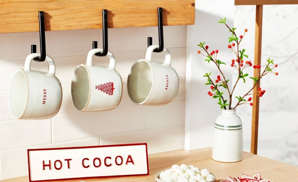 mugs hanging on a wall with a hot cocoa sign on the counter beneath them