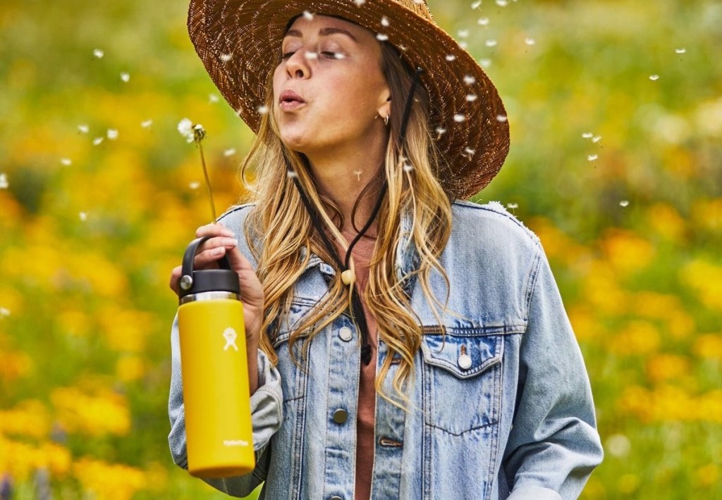 woman blowing on a dandelion while carrying a Hydro Flask