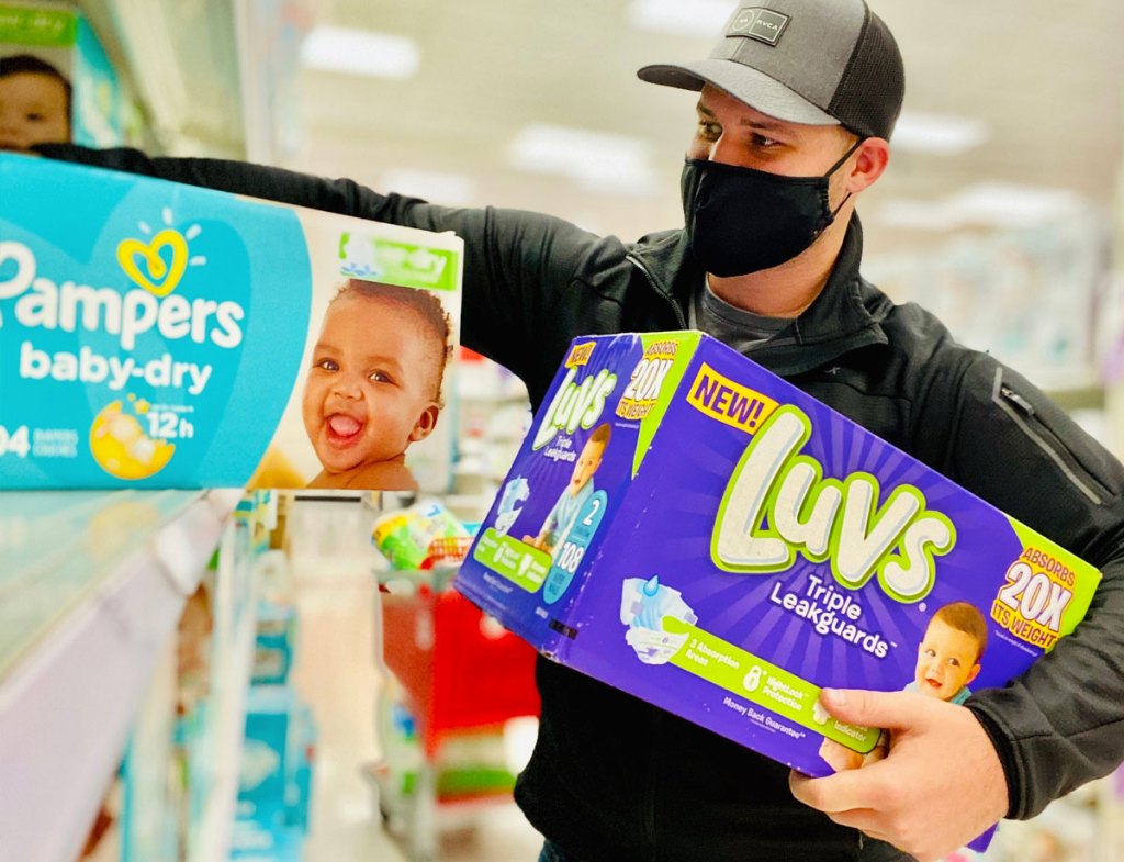 man wearing hat, black jacket, and black face mask grabbing boxes of luvs and pampers diapers off target shelf