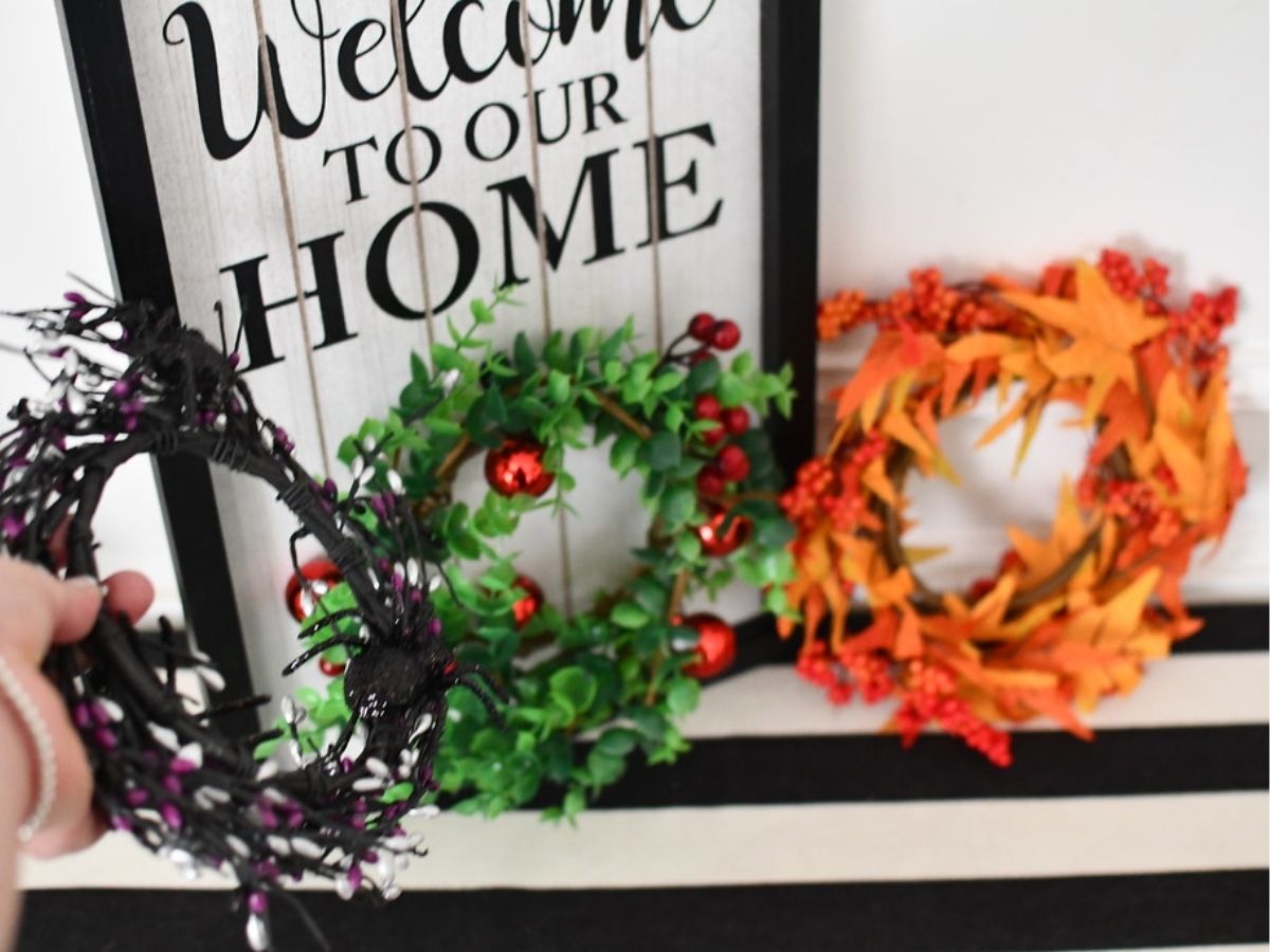 hand holding purple wreath with Christmas and fall wreath next to it