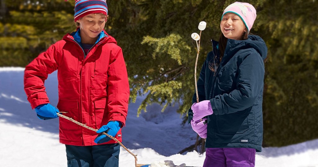 two kids wearing winter jackets and accessories while in snow roasting marshmallows