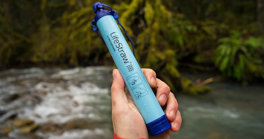 Hand holding a blue LifeStraw personal water filter near water, outdoors