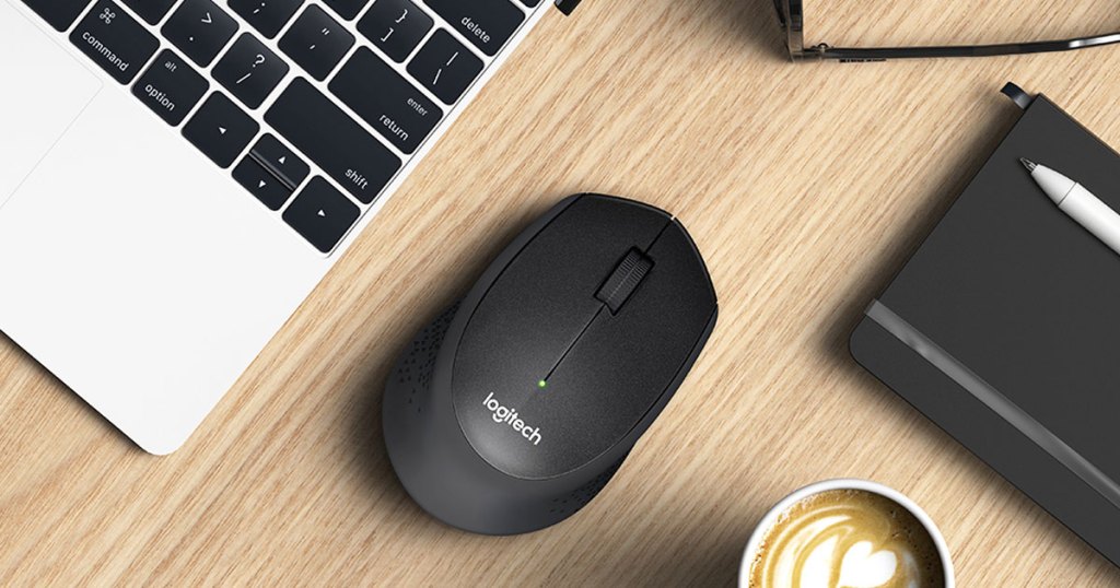 black logitech wireless mouse on wood table next to laptop and cup of coffee