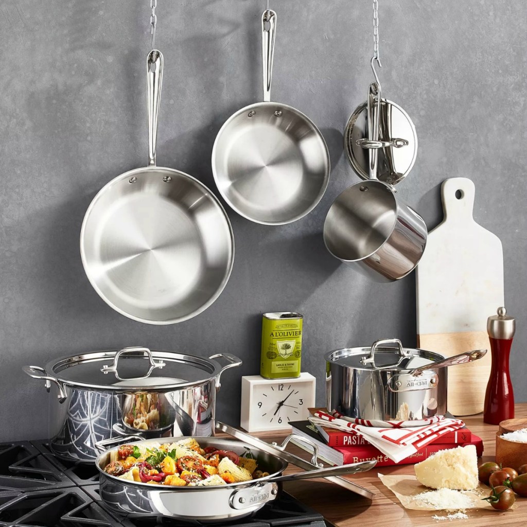Large stainless steel cookware set on a counter and hung on a gray wall