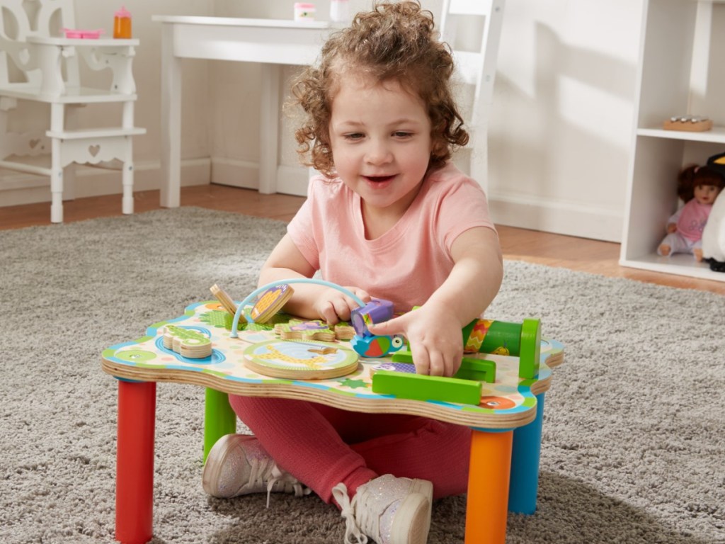 little girl sitting on a playroom floor playing with the melissa & doug jungle set