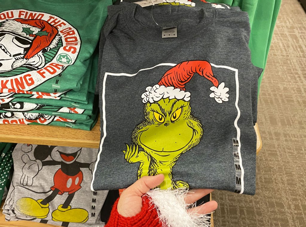 person in red and white santa glove holding folded grey grinch graphic tee