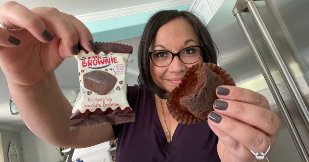 woman holding Mr. Brownie bite package in one hand and the brownie in the other