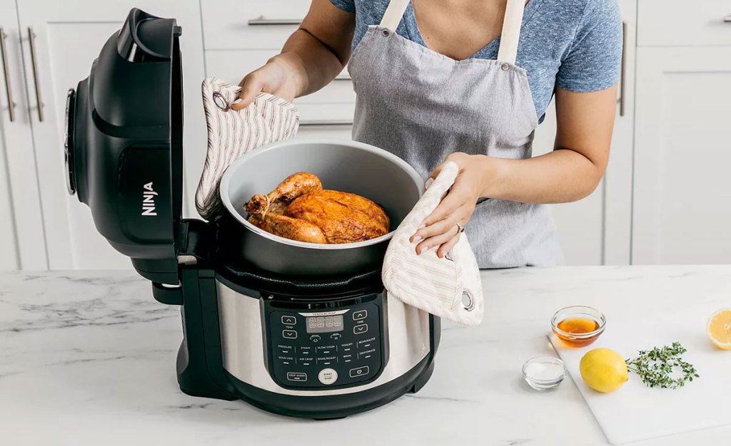 woman lifting out inner pot of ninja foodi pressure cooker with whole roast chicken inside