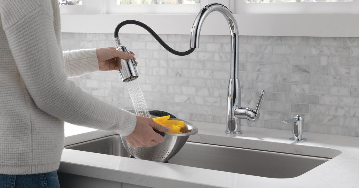 woman using a pull-down faucet to rinse a bowl of sliced fruit in a sink