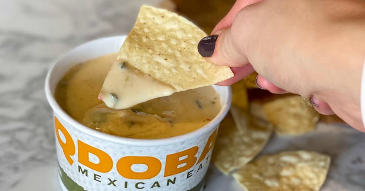 Woman's hand holding a tortilla chip dipping it in queso