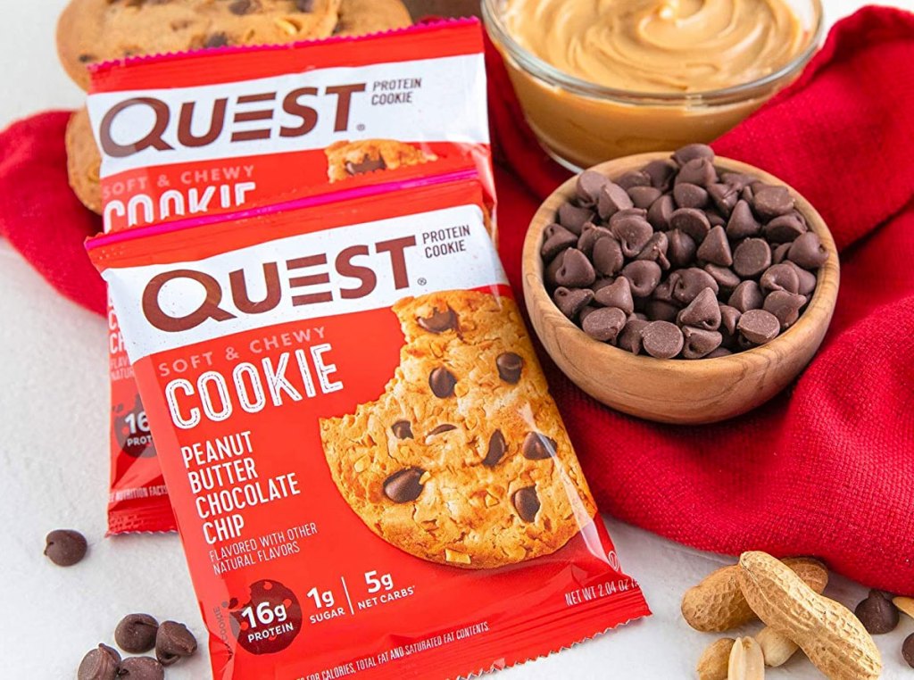 two red packages of quest peanut butter chocolate chip cookies on table near bowls of peanut butter and chocolate chips