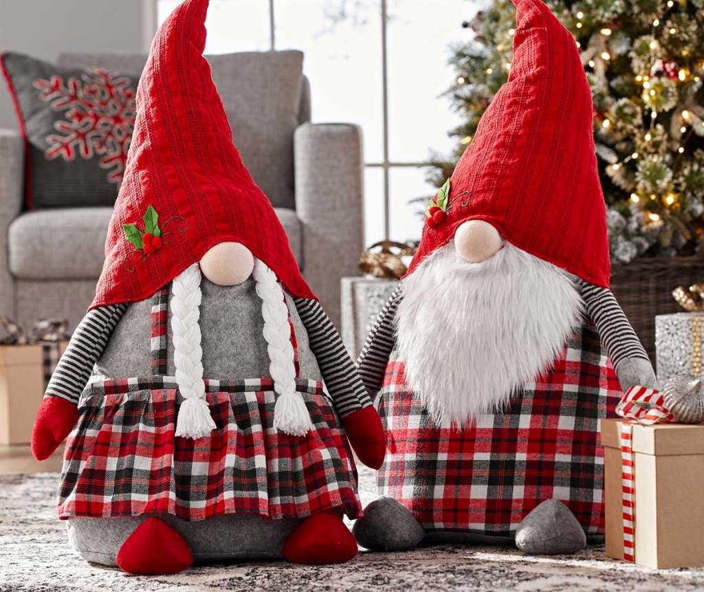 set of two oversize christmas themed gnomes on floor near christmas tree