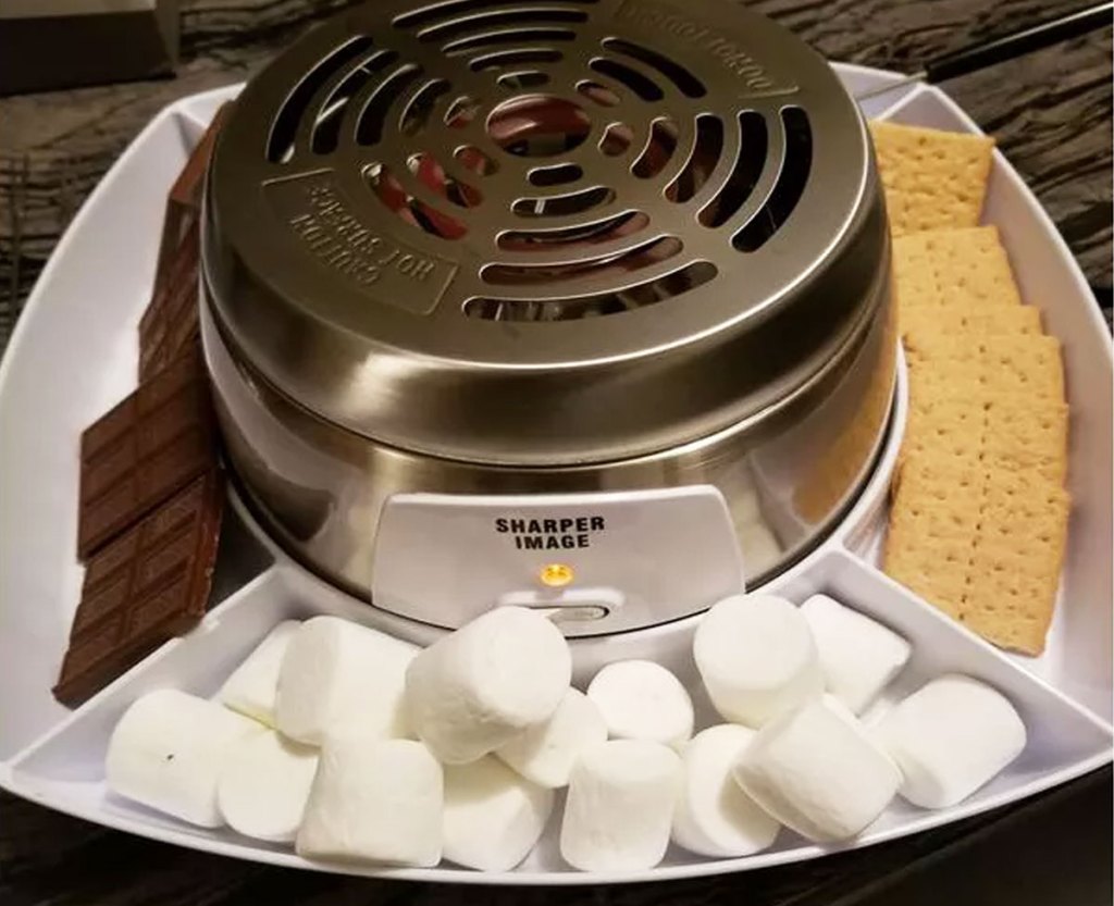 stainless steel smores grill with chocolate, marshmallows, and graham crackers in tray around it