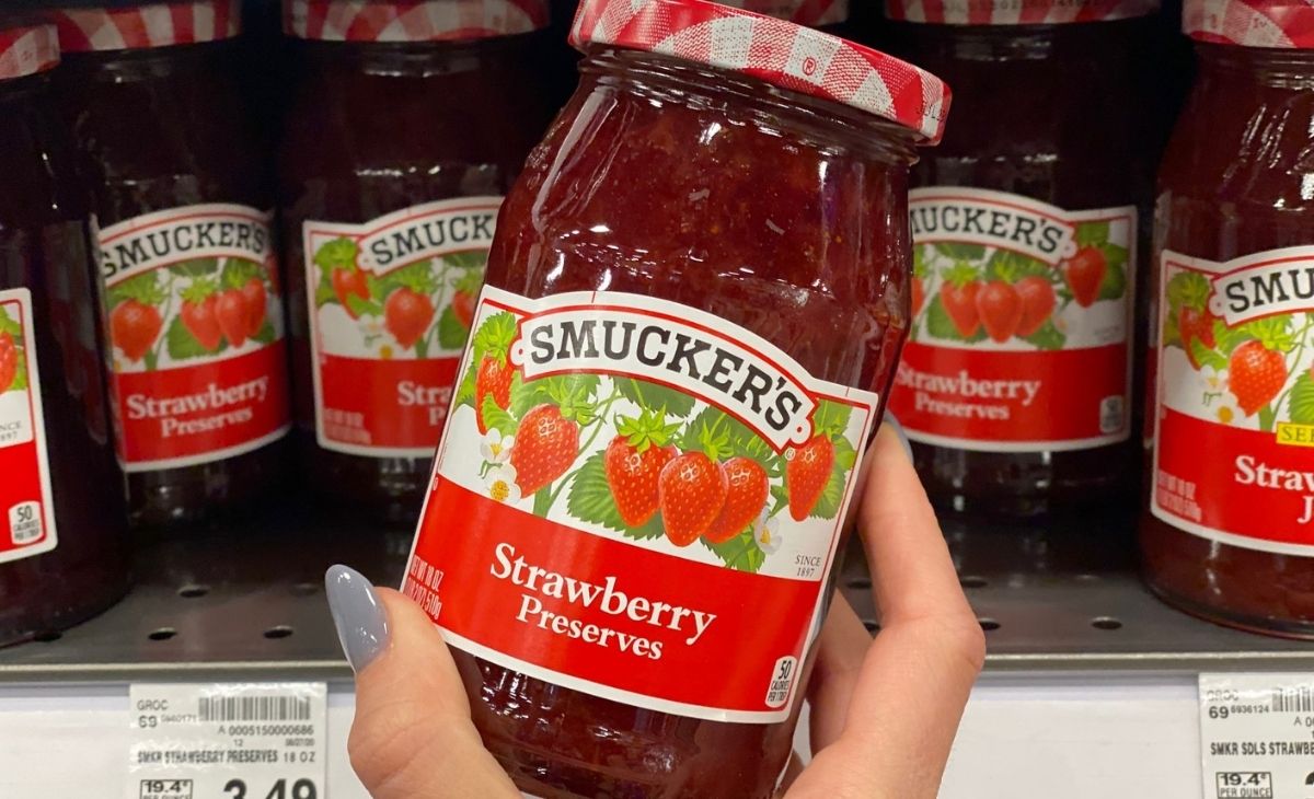 A hand holding a jar of Smuckers preserves in front of a store shelf