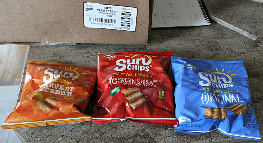 three bags of chips on counter, shipping box, pad and pen