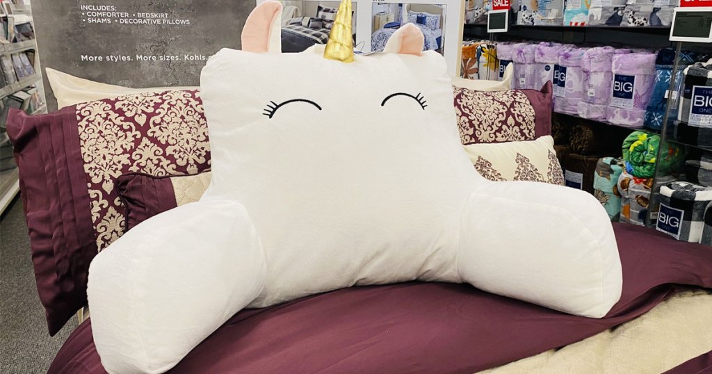 white unicorn face backrest pillow with gold horn sitting on a bed