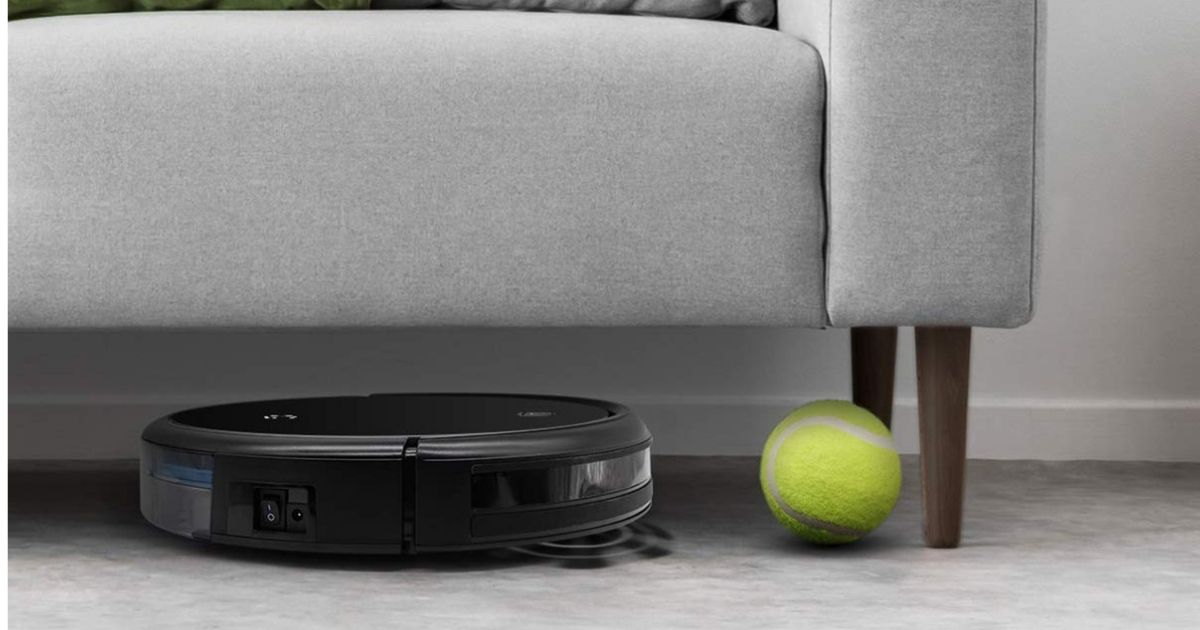 robotic vacuum cleaning under gray couch by green tennis ball