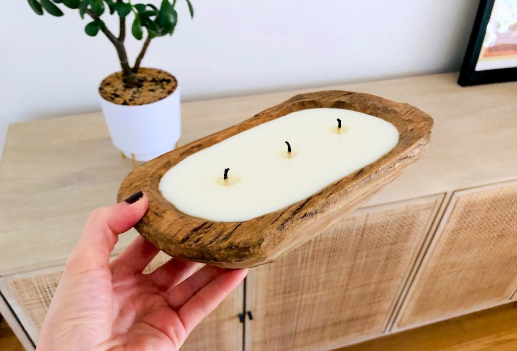 hand holding wooden bowl soy candle in front of caned console table