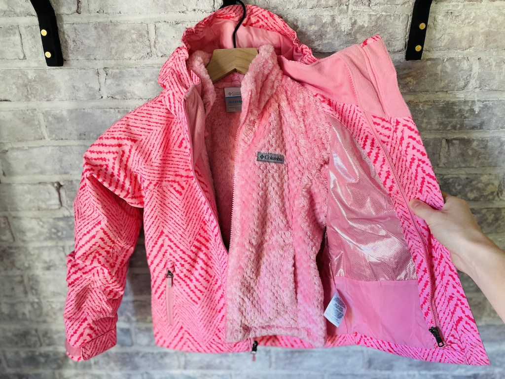 hand holding open pink kids jacket hanging on hook