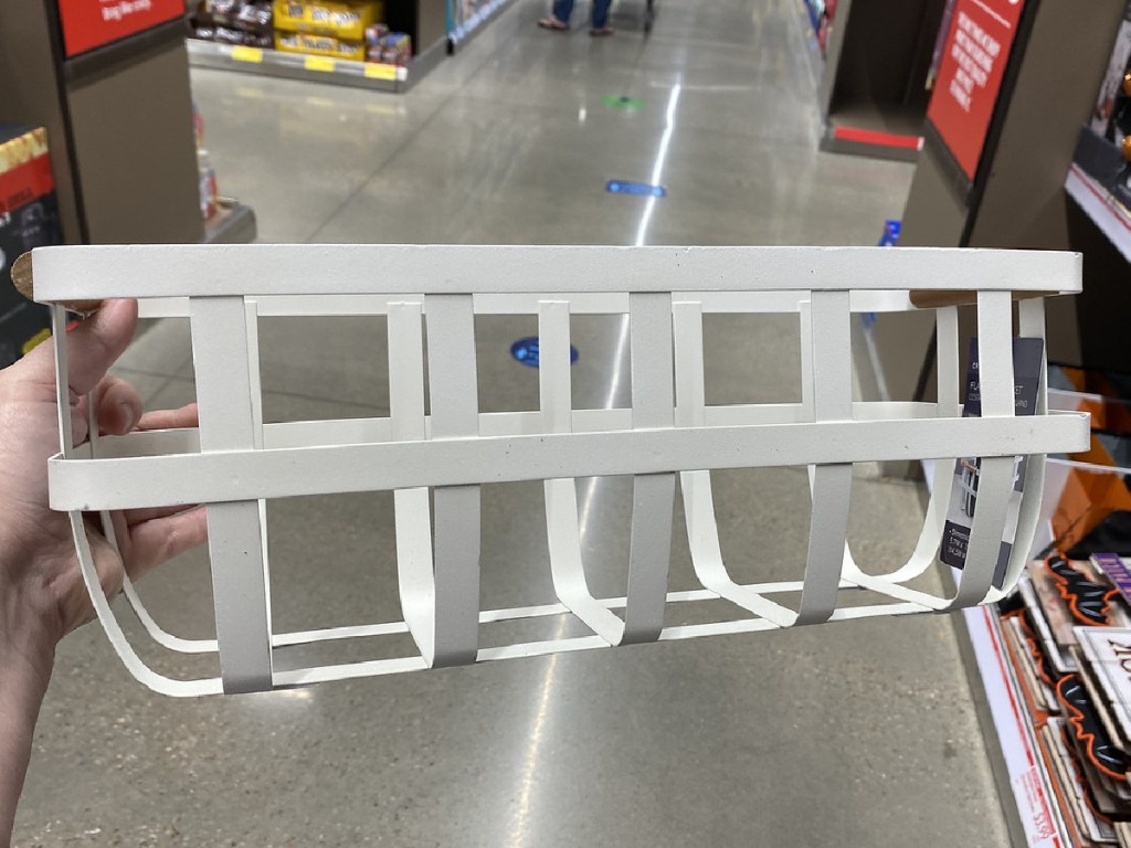 hand holding white wire basket in store aisle
