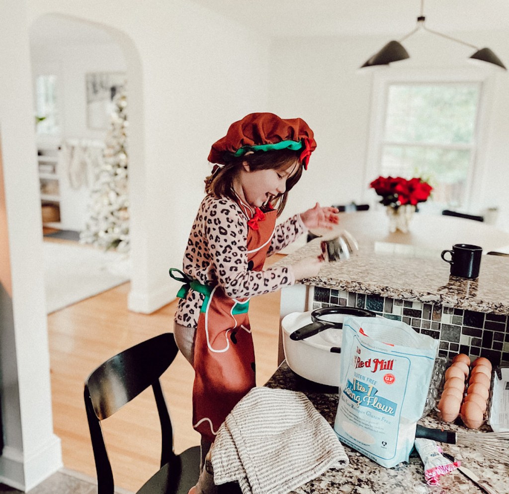girl wearing gingerbread outfit standing in chair baking