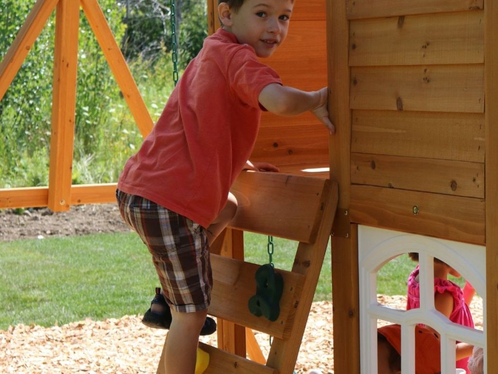 boy climbing ladder attached to wooden playhouse