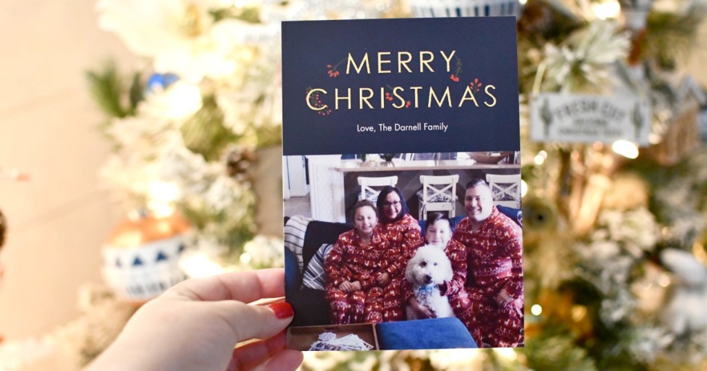 person holding up a Christmas photo card in front of tree