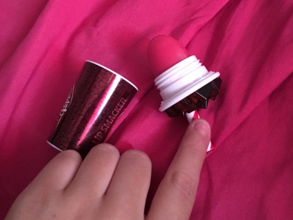 Hand touching balm part of lip smackers dr pepper lip balm with pink backdrop
