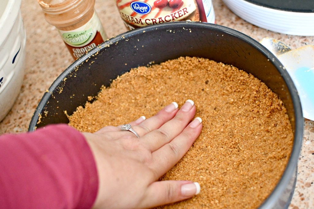 pressing a graham cracker crust cheesecake