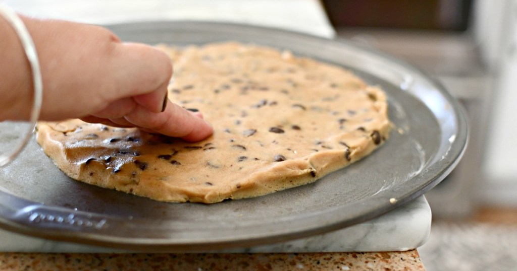pressing cookie dough on a pizza pan